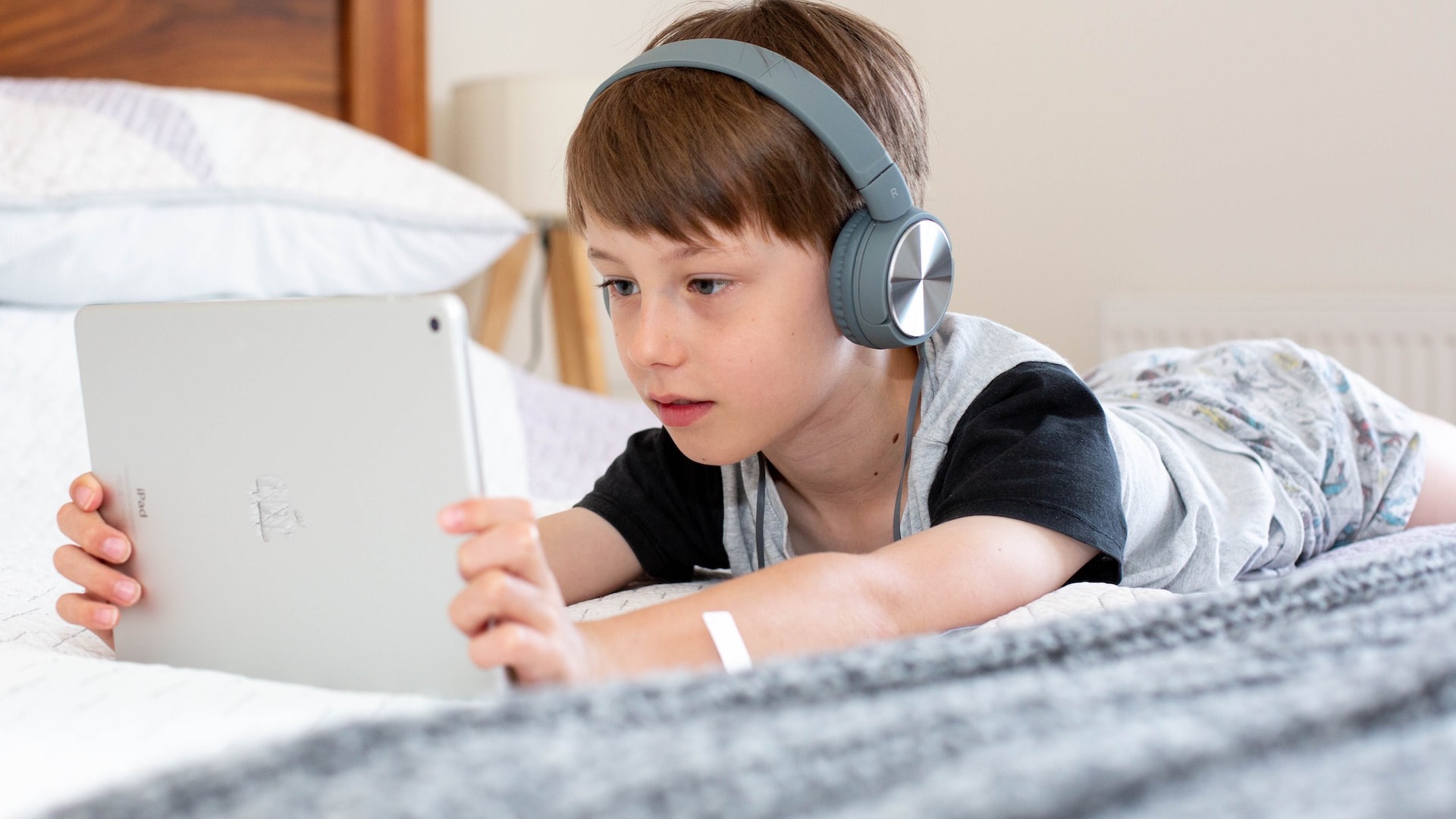 boy in blue shirt wearing headphones lying on bed